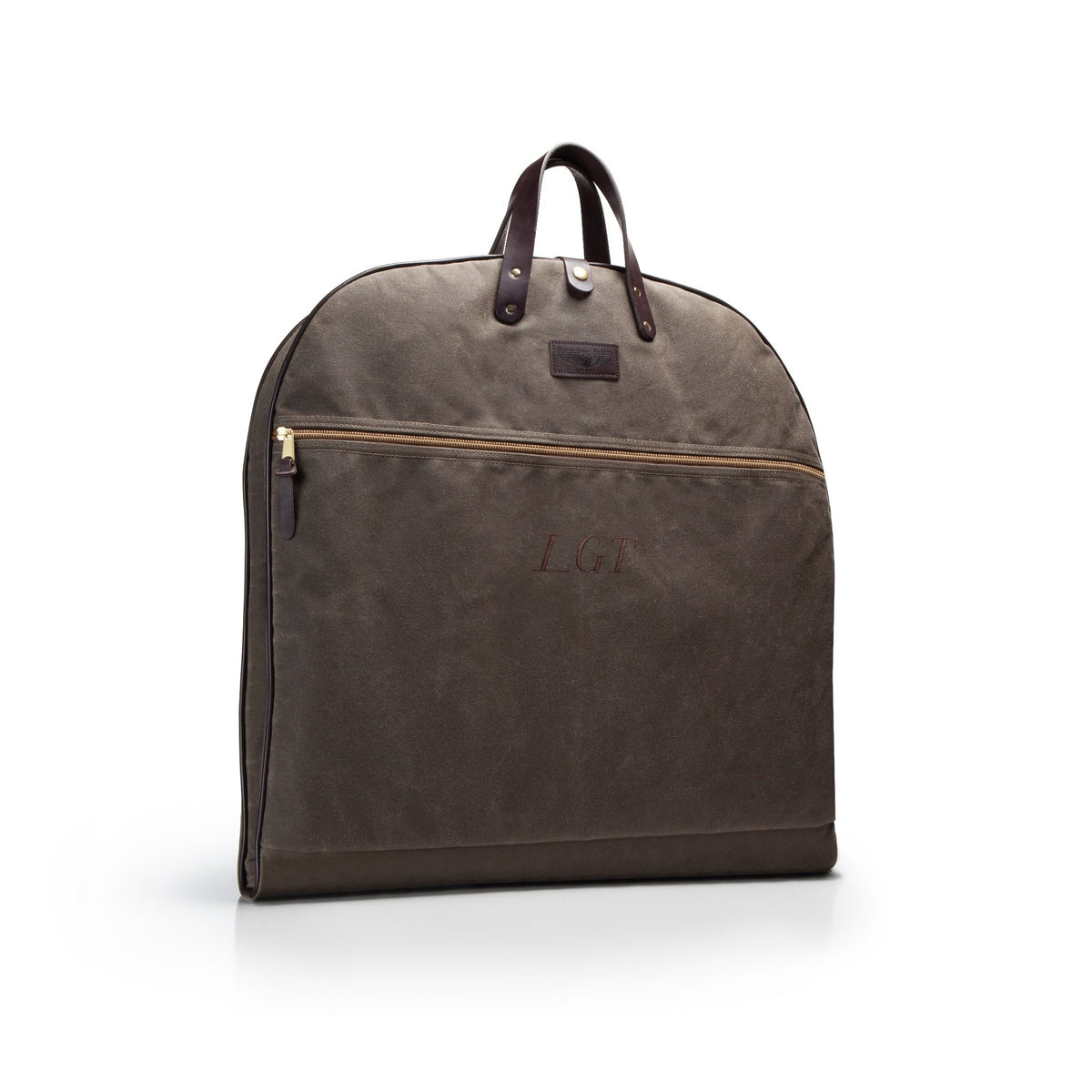 A dark brown waxed canvas garment bag that is monogrammed with LGT with dark brown leather handles and a brass zipper, shown on a clean white background.