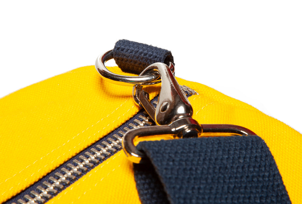 Close-up of a yellow bag with a black strap and silver zipper on a white background