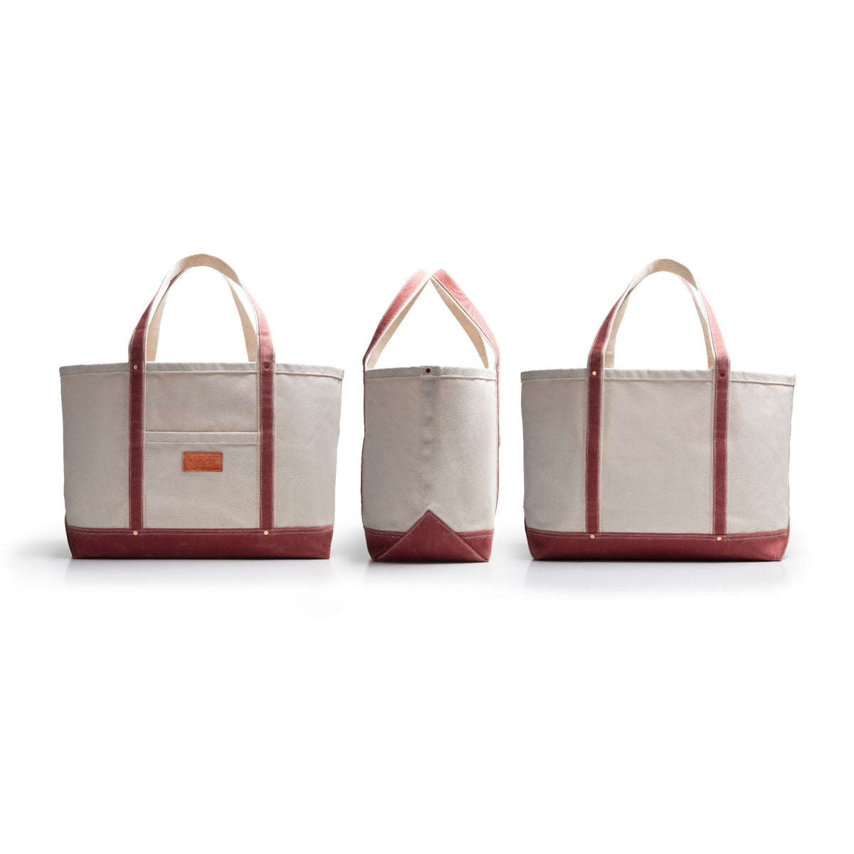 Three angles of canvas tote bags with dark red accents and handles and bottom with tan leather patch on a white background that is front, side and back facing angles