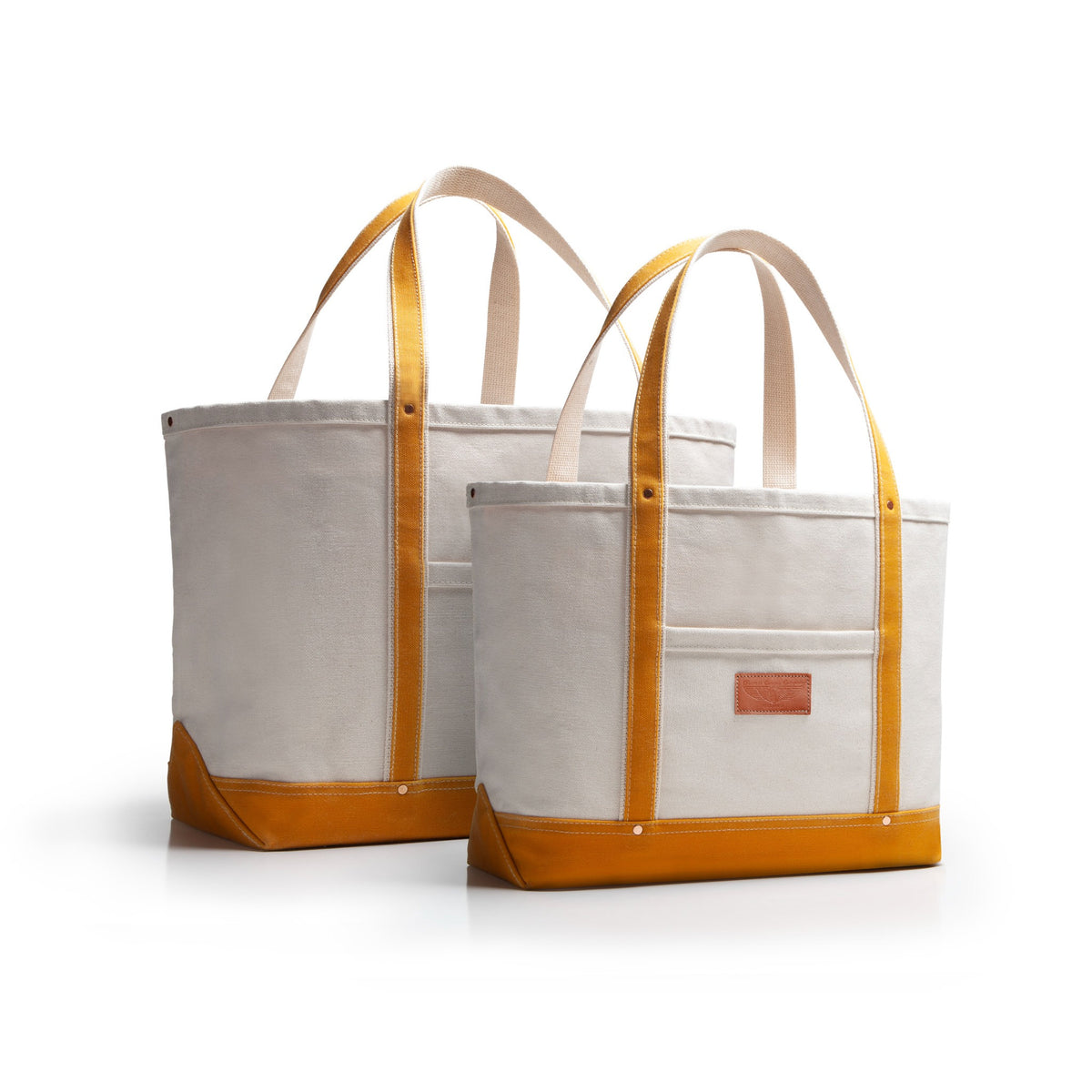 Two canvas tote bags with yellow accents and handles and bottom with tan leather patch on a white background