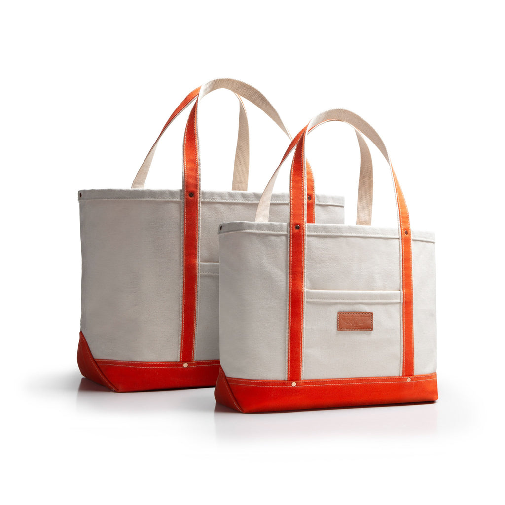 Two tote bags with orange accents and handles and bottom with tan leather patch on a white background