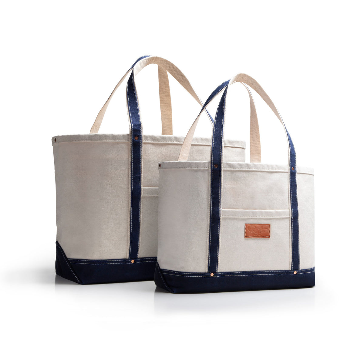Two tote bags with navy blue accents and handles and bottom with tan leather patch on a white background