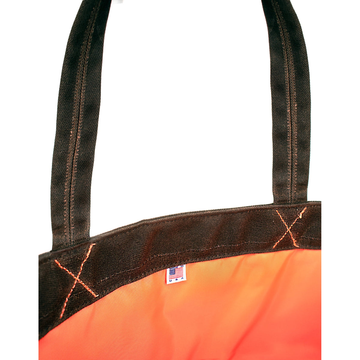 Close-up of a bright orange bag with dark brown webbed handles and trim, featuring contrast stitching and a small made in USA flag tag near the top.