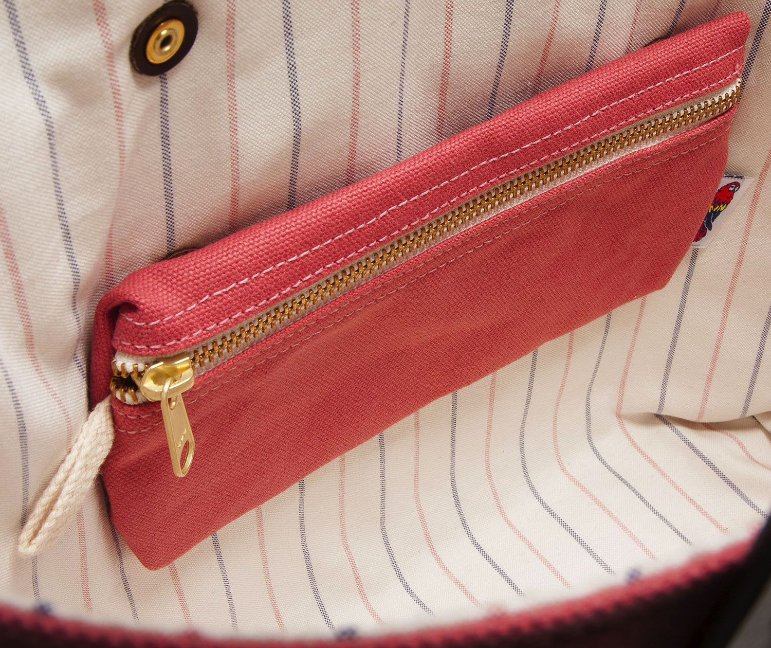 Red pouch with gold zipper on a striped fabric background