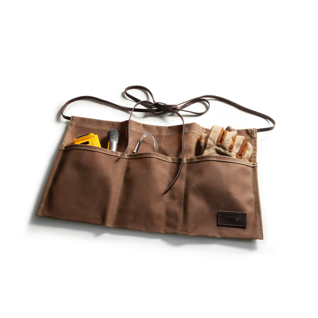 A brown canvas tool roll with multiple pockets, shown open on a white background. The pockets contains various hand tools and gloves, and has a small black brand patch on the lower right corner.