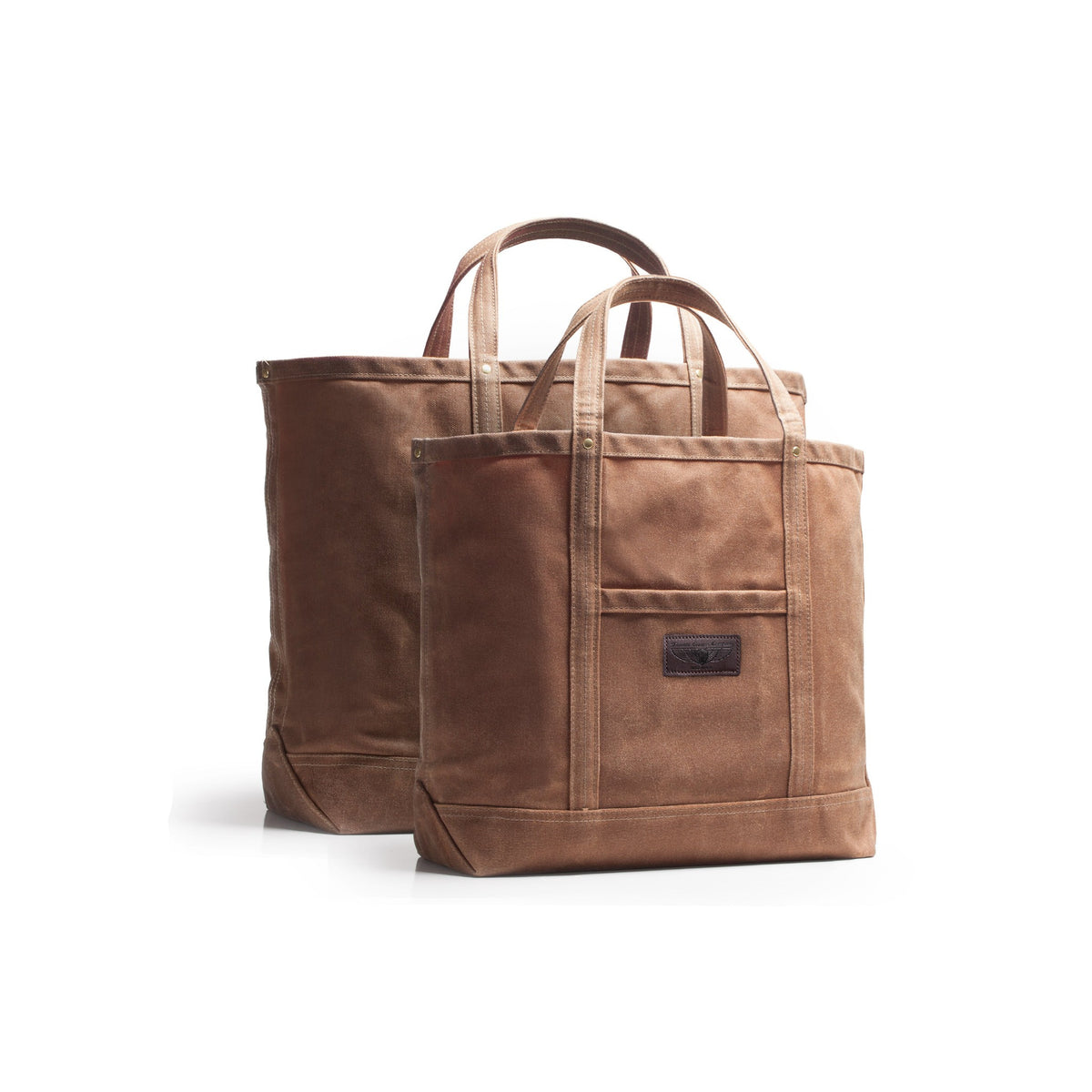 A brown waxed canvas tote bag with dual top handles and a dark brown leather brand label and front pocket, shown in front of a second larger matching bag on a clean white background.