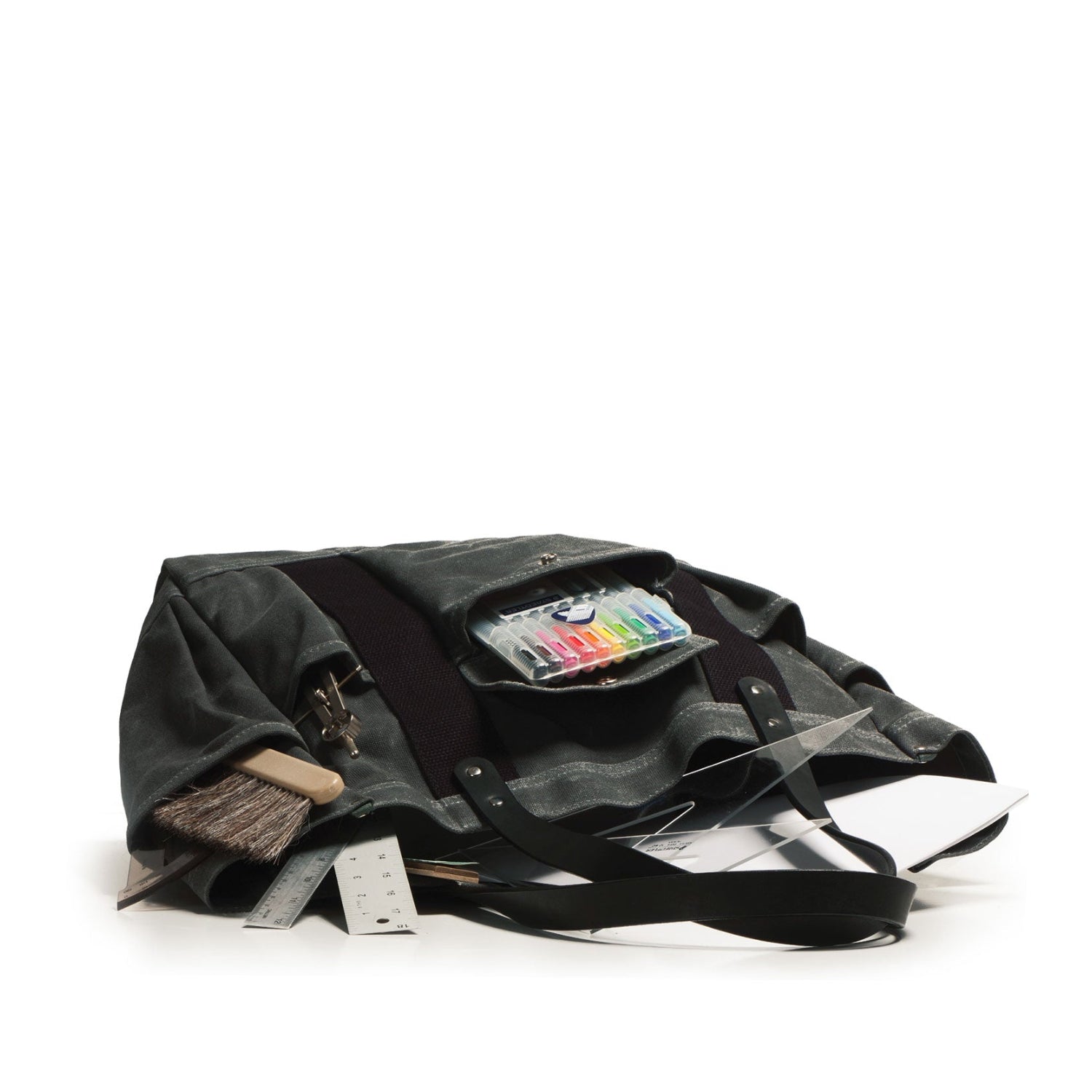 Black leather bag with various items including a brush and colorful packaging on a white background