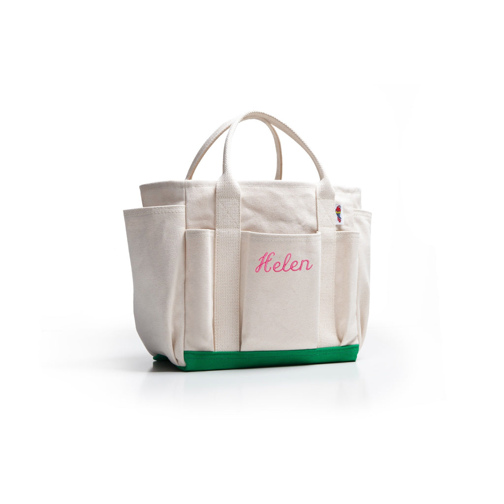 An off-white canvas tote bag with a green base and pink embroidered name 'Helen' on the front pocket, set against a plain white background.