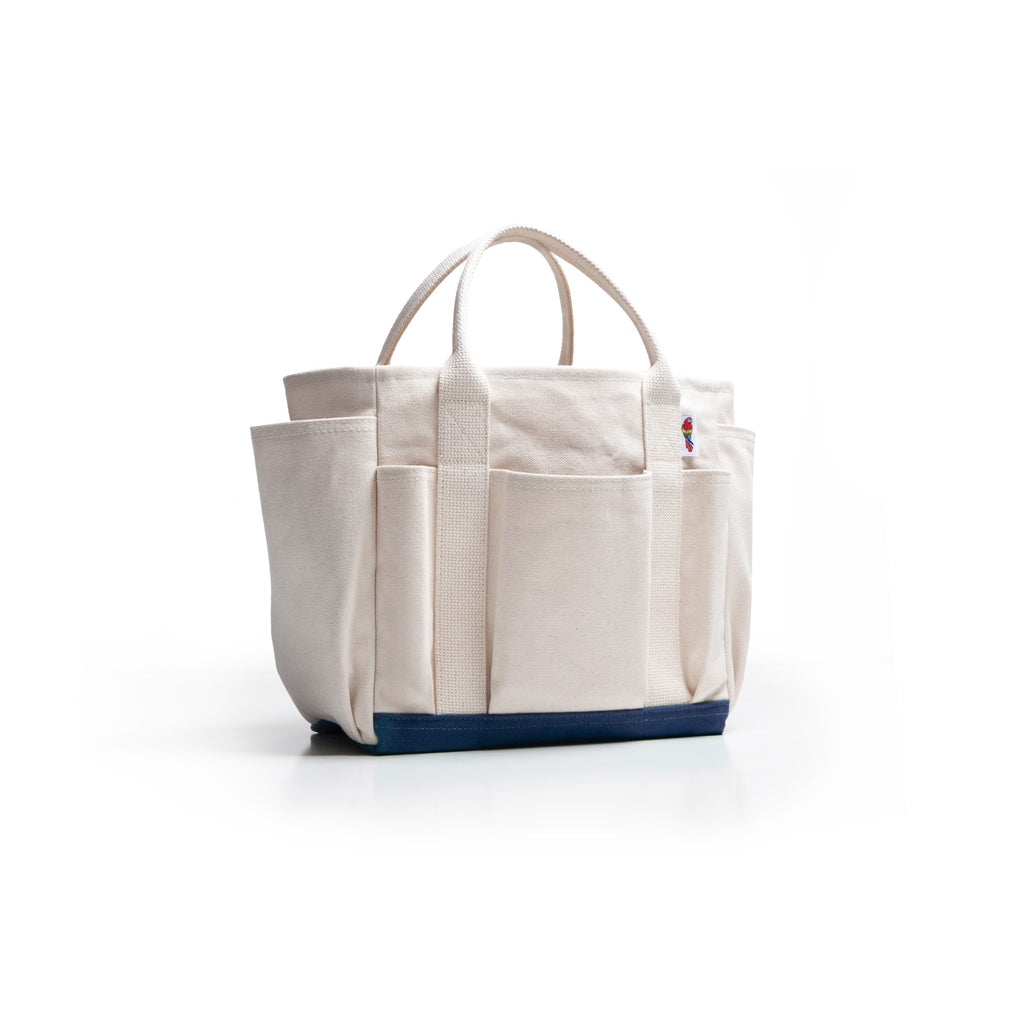 An off-white canvas tote bag with multiple front pockets and a dark navy blue base, shown on a clean white background.