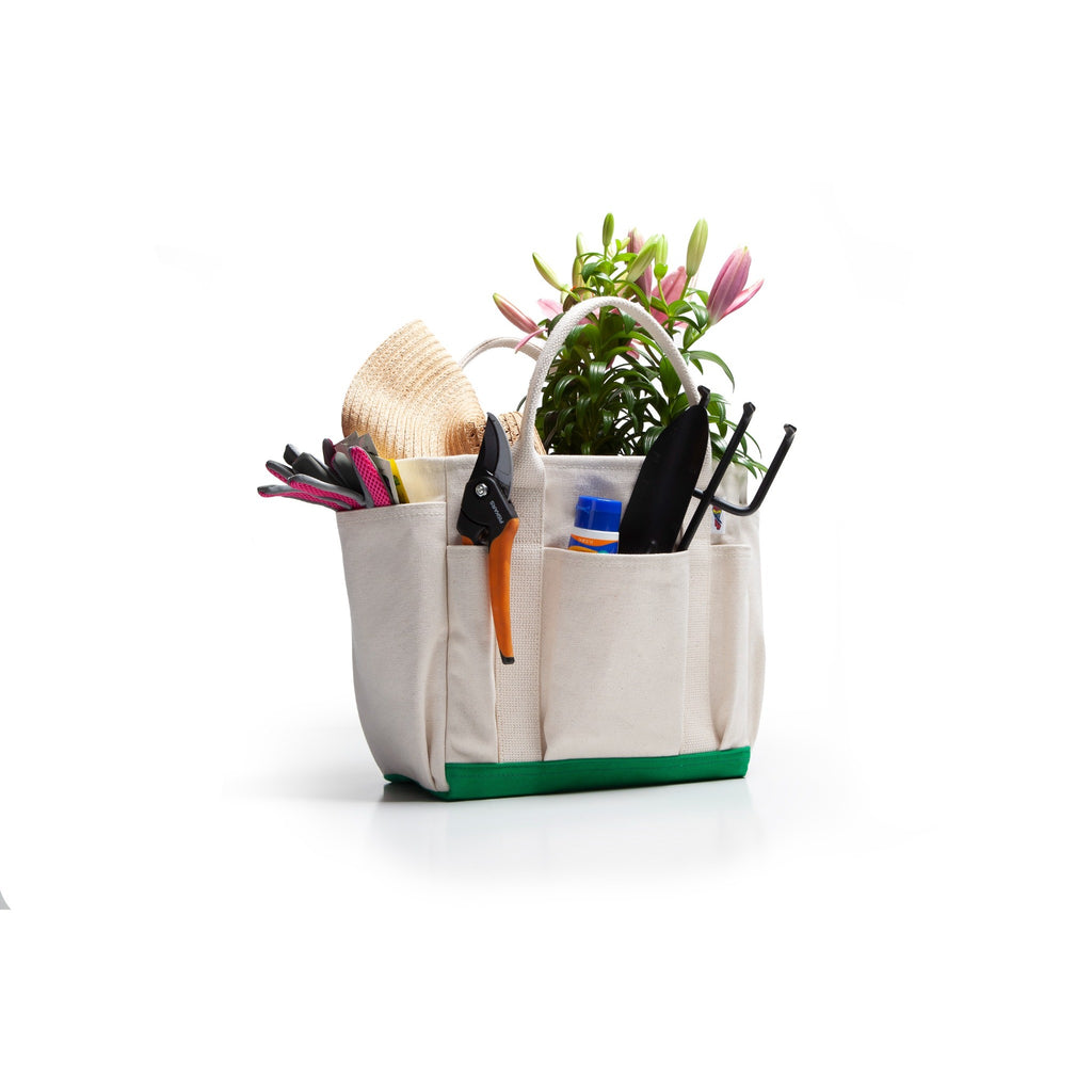 An off-white canvas garden tool caddy tote bag with a green bottom base, filled with gardening tools and a small potted plant, on a white background.
